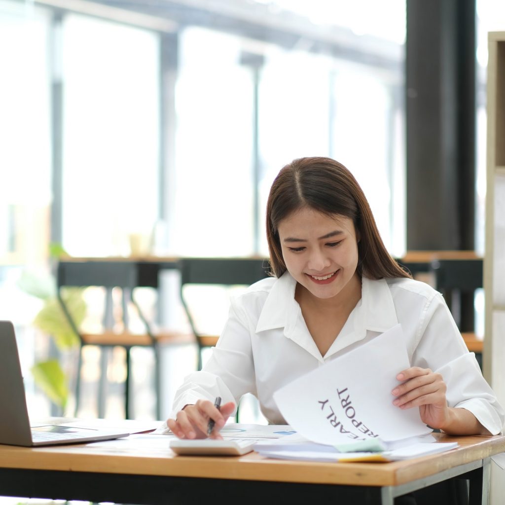 Smiling beautiful Asian businesswoman analyzing chart and graph showing changes